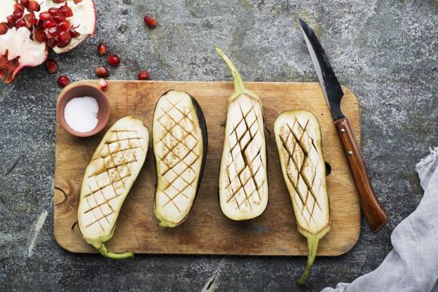Fresh ripe eggplants sliced with a knife and sprinkled with salt before grilling for a side dish on a gray granite background. Top View.