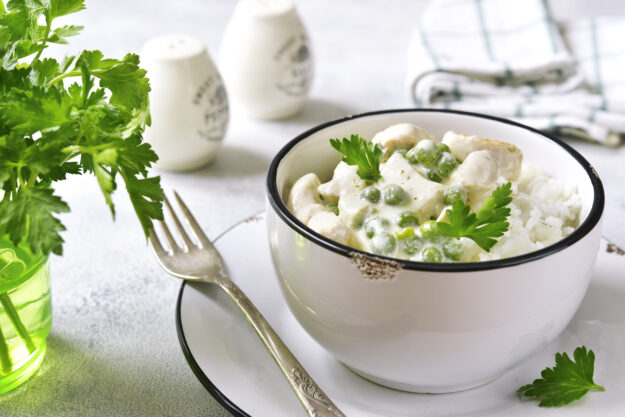 Chicken fricasse with green pea served with boiled rice on a light background.